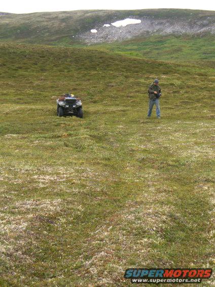 ATV parked on grassy hill with person standing nearby