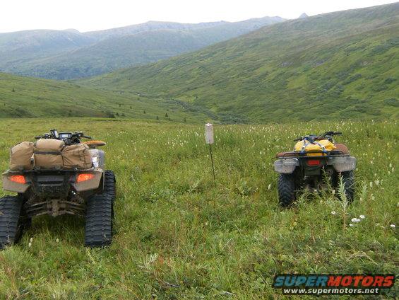Two ATVs parked in a wide, grassy valley with mountains in the background