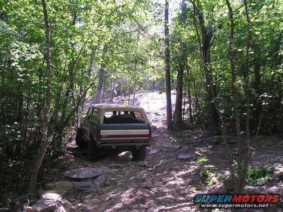 1989 Ford Bronco driving on a rocky, wooded trail