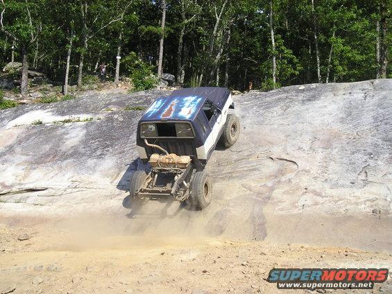 1989 Ford Bronco climbing a steep, dusty rock face with trees in the background