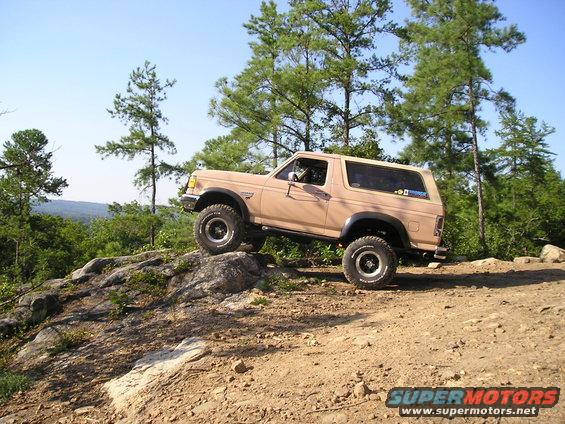 Tan Ford Bronco with off-road tires climbing a rocky incline