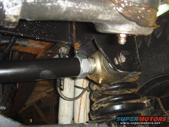 Black suspension arm with silver nut connected to gold bracket, near black coil spring and white shock absorber