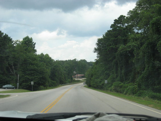 Two-lane road curves through a wooded area with a speed limit sign visible