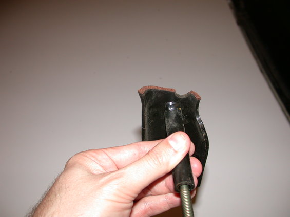 Hand holding a black automotive part with a metal threaded rod