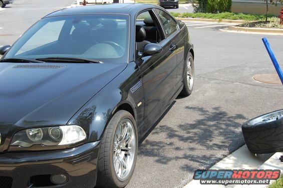 Black coupe parked on asphalt, front quarter view. Chrome wheels, side vent visible