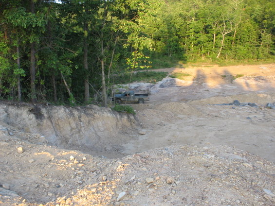 Green pickup truck parked on dirt road near trees