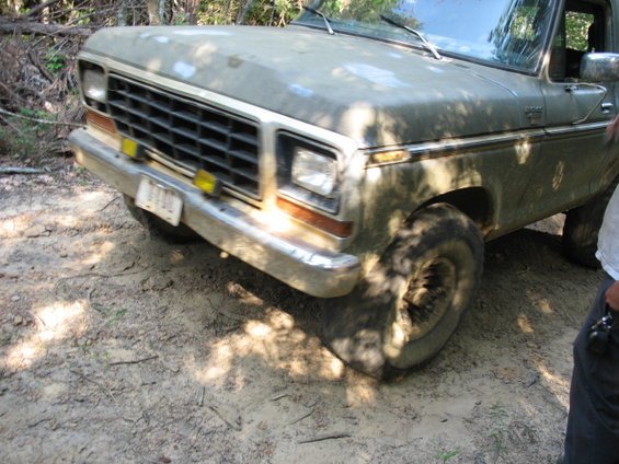 1978 Ford Bronco, dusty olive green, front 3/4 view, off-road tires, chrome bumper, yellow fog lights