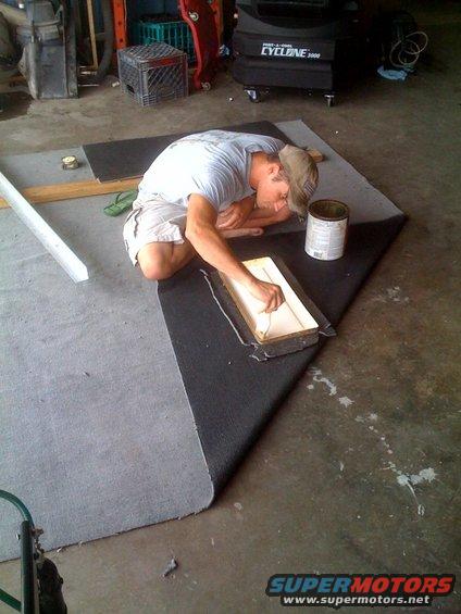 Guy in a garage working on a piece of carpet with a can of glue