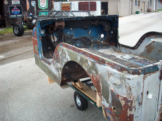 1978 Jeep CJ5 body on a dolly, showing rust and peeling paint, with a roll cage frame attached