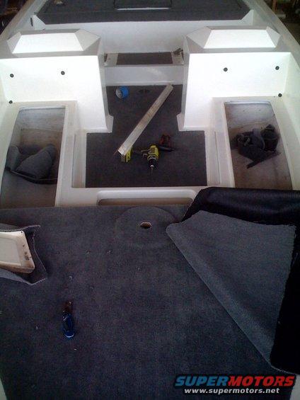Boat interior with dark carpet, white fiberglass, and a drill. Some seats are visible
