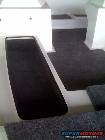 Interior of a boat with dark carpeted floor and white molded seating areas
