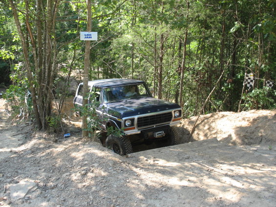Dark blue 1978 Ford Bronco navigating an off-road obstacle, front-right tire deep in a rut