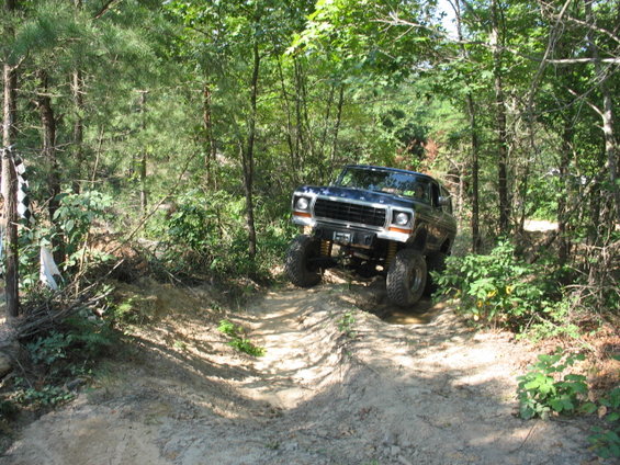 Dark blue Ford Bronco climbing a dirt trail in a wooded area