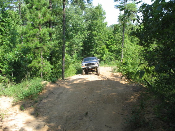 Blue pickup truck on dirt road, front view. Lifted suspension, off-road tires