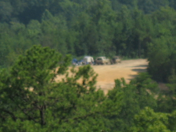 Several vehicles and tents are parked in a dirt clearing surrounded by trees