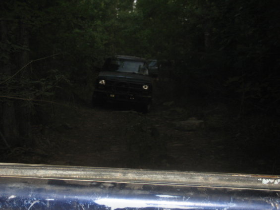 Dark 1978 Ford Bronco on a dirt path in a wooded area, front view