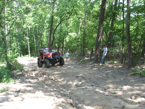 Red Jeep Wrangler driving on a rocky, wooded trail
