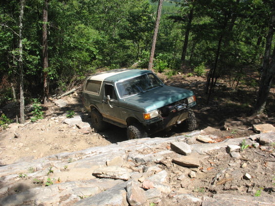 Green Ford Bronco with a white top navigating a rocky trail