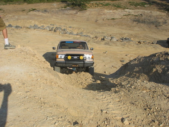 Tan Ford Bronco driving through dirt terrain with smiley face lights on the bumper