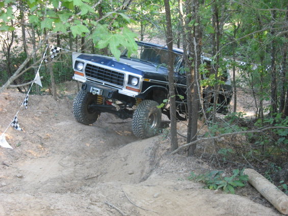 1978 Ford Bronco climbing a dirt hill with trees on either side