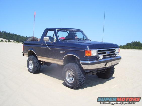 Dark blue 1991 Ford Bronco with tan trim, lifted, on sand