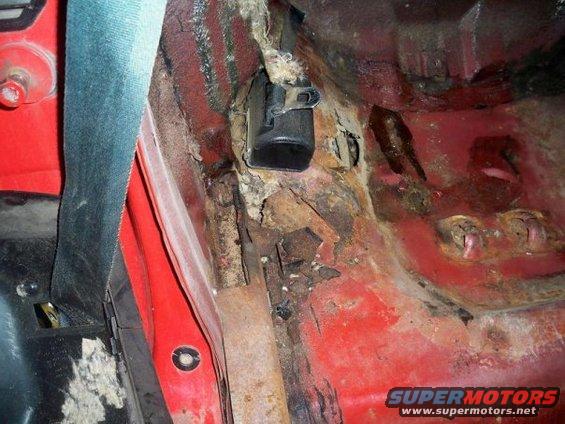 Close-up of heavily rusted floor pan and seatbelt anchor inside a car