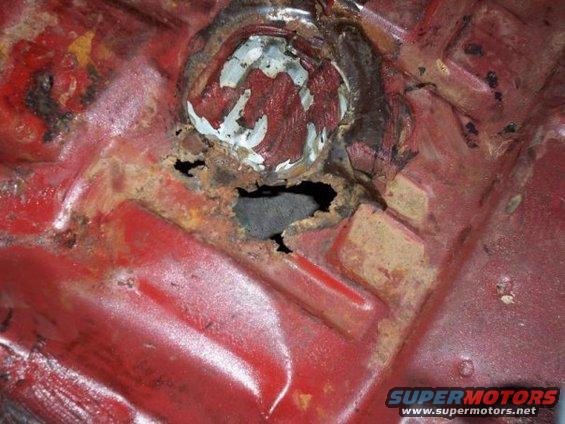 Rusted floor pan with hole and red paint