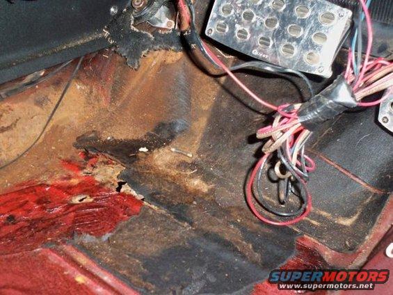 Car's floor pan is rusted out, with exposed wiring and pedals visible