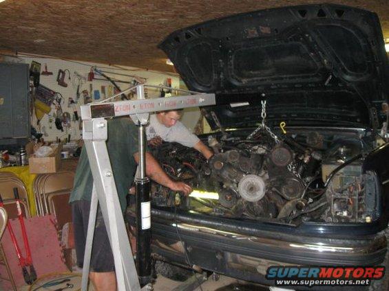 Engine being lifted out of a dark-colored SUV with an engine hoist