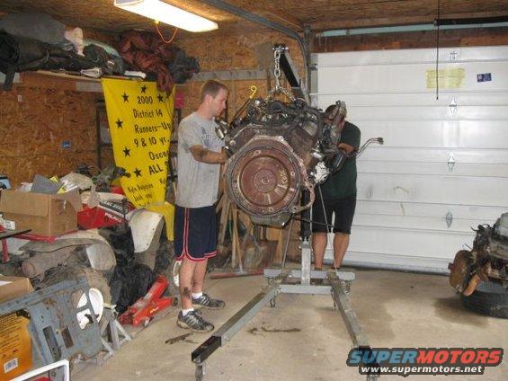 Engine on an engine hoist in a garage with two men working on it