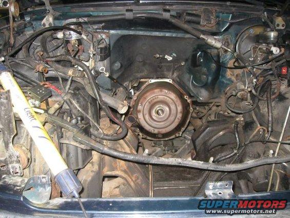 Engine bay with transmission torque converter visible. Yellow light tool in frame