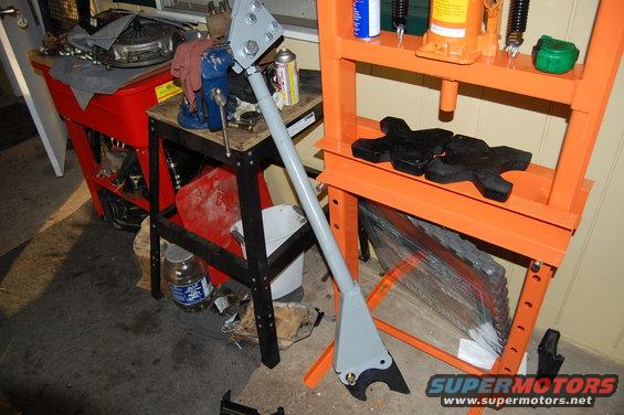 Gray metal part clamped in vise near hydraulic press and tool cart