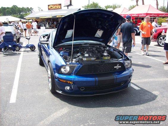 Blue Ford Mustang with hood open, showing engine. Two black stripes on hood and front