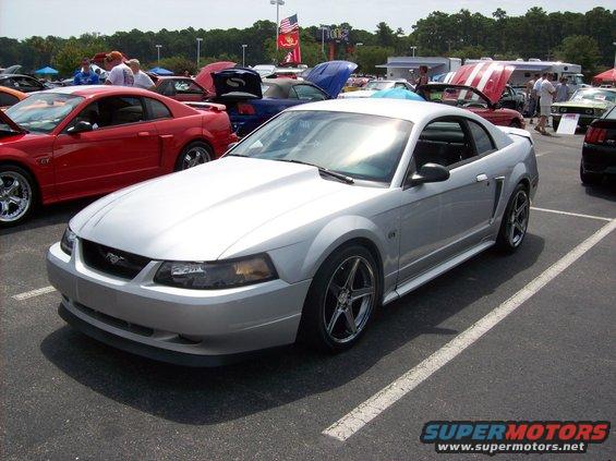 Silver Ford Mustang coupe with aftermarket hood and wheels parked in a lot