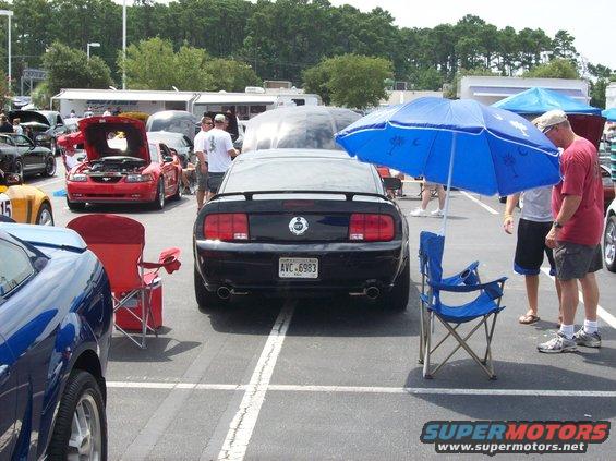 Black 2007 Ford Mustang rear view, parked at car show with other vehicles and people