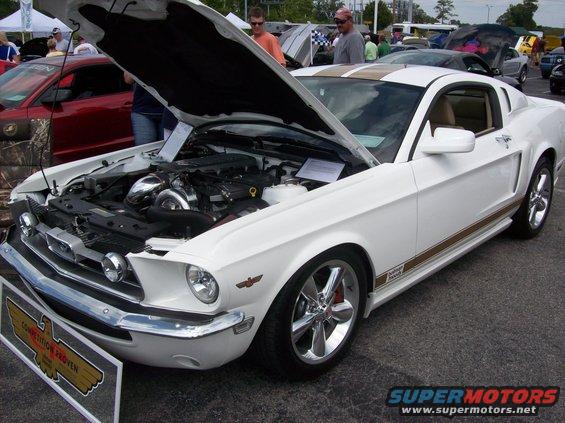 White 1967 Ford Mustang with gold racing stripes and hood open, showing a custom engine