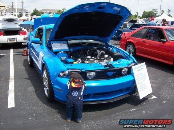 2007 Ford Mustang with hood open, child in overalls looking at engine. Red Mustang in background