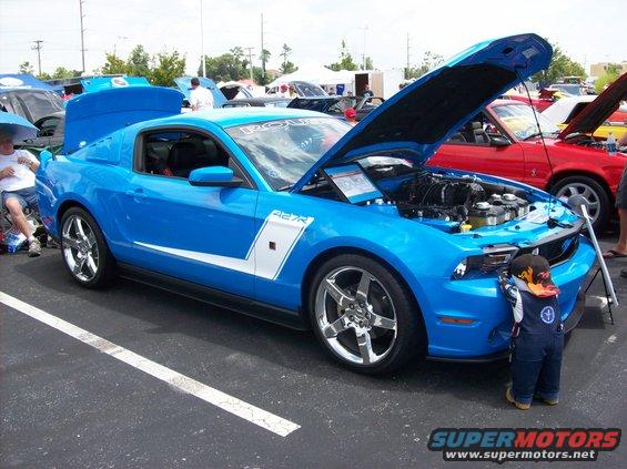 Blue 2007 Ford Mustang with hood open, a kid is looking at the engine. Another red car is parked next to it