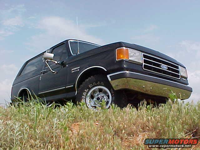 1989 Ford Bronco parked on a grassy hill under a cloudy sky