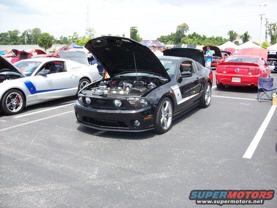 Black 2007 Ford Mustang parked with hood open, showing engine. Silver Mustang and red Mustang visible in background