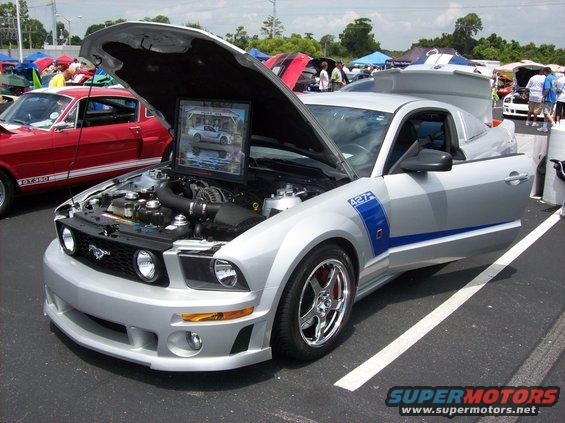 Silver 2007 Ford Mustang with hood open, showing engine and a framed picture. Blue stripe on side