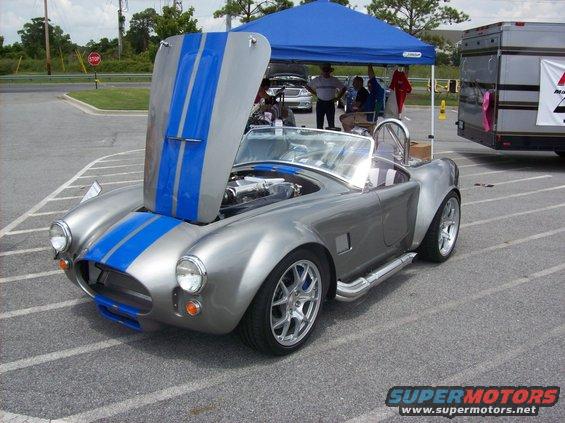 Silver Shelby Cobra replica with blue stripes, hood open showing engine