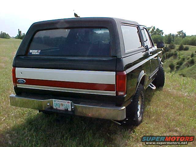 Black Ford Bronco parked on a grassy hill, rear view. Has a red and white stripe on the tailgate