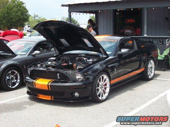 Black 2007 Ford Mustang with orange stripes, hood open, showing engine