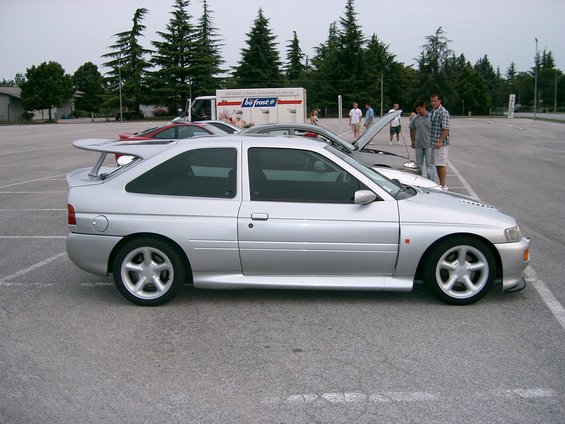 Silver hatchback with a large rear spoiler, side view. Appears to be a Ford Escort RS Cosworth
