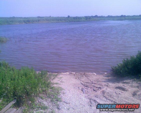 Water body with shore and vegetation, Supermotors.net logo visible