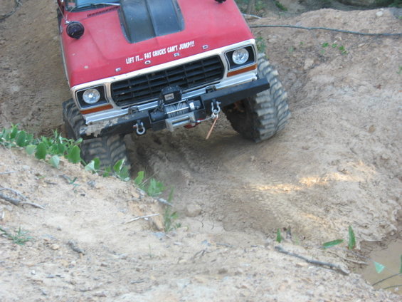 Red Ford truck with large tires climbing a dirt hill. Text on hood says 'LIFT IT... FAT CHICKS CAN'T JUMP!!!'