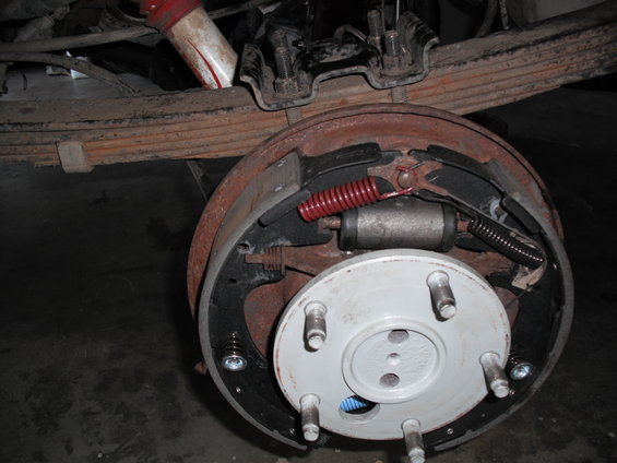 Rear drum brake assembly with new pads and springs. Leaf springs and shock absorber visible above