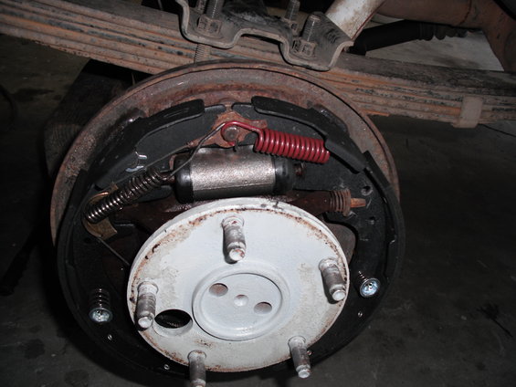 Drum brake assembly with rusted drum, new brake shoes, and red spring. Leaf springs visible above