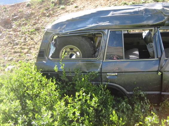Dark SUV with a dented roof and broken rear window, spare tire visible inside. "Land Cruiser" text visible on the side